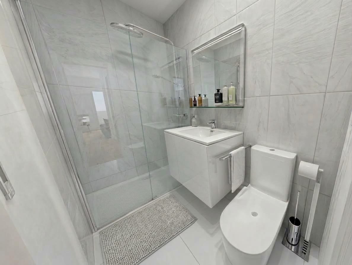 Baño reformado con plato de ducha a ras de suelo y azulejo tipo mármol